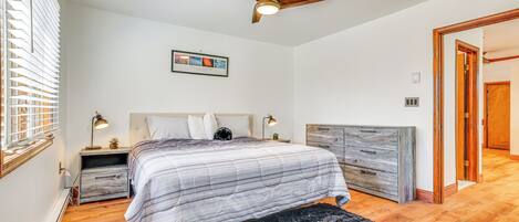 A bedroom with a bed, a ceiling fan, a nightstand, a dresser, and a framed picture on the wall.