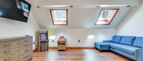 A room with a wooden floor, a blue sofa, a TV mounted on the wall, and two skylights.
