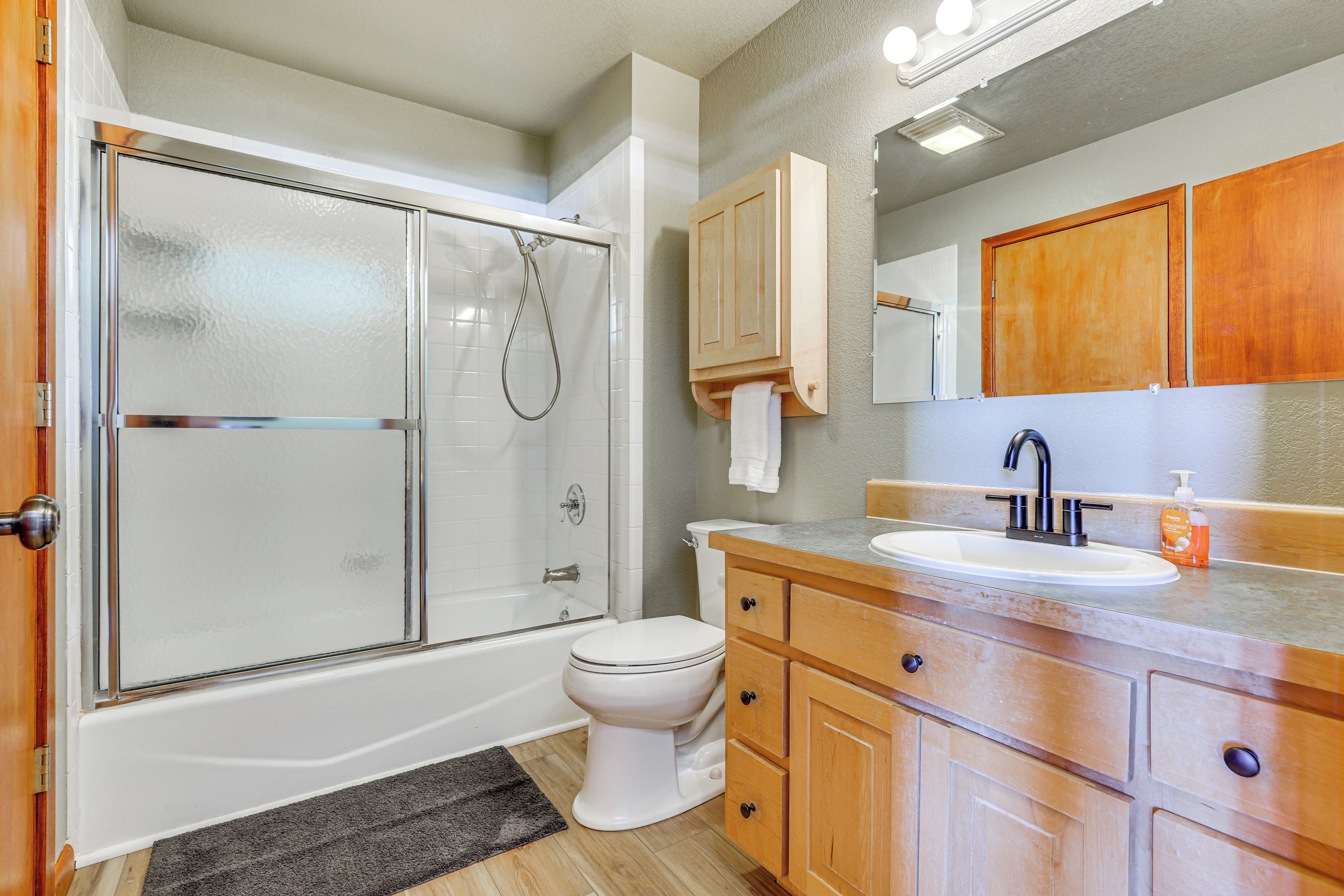 Un bagno con cabina doccia in vetro, un WC bianco, mobili in legno e un lavabo con specchio sopra.