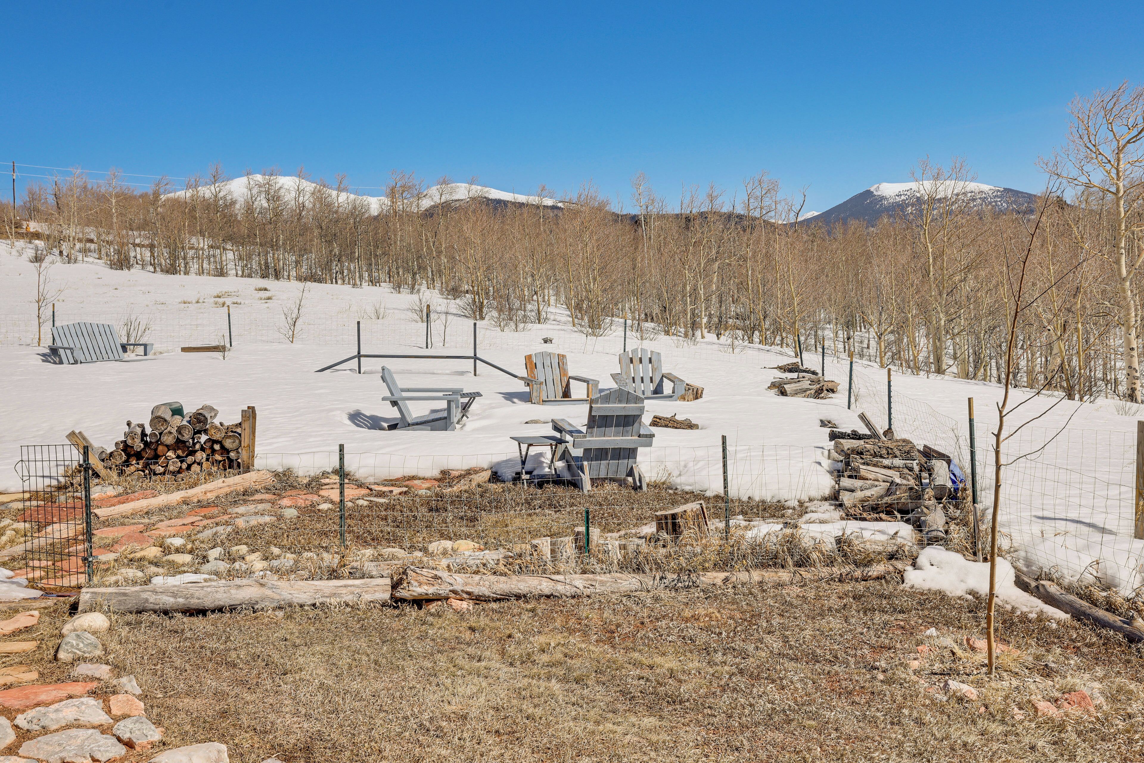A snowy outdoor area with a wooden deck, chairs, and a pile of firewood.
