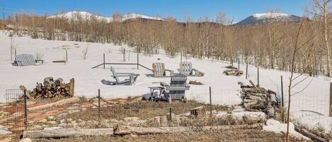 A snowy outdoor area with a wooden deck, chairs, and a pile of firewood.
