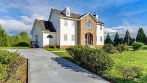 Une maison à deux étages, avec une partie en briques et un revêtement extérieur blanc, un porche à l’avant et une allée menant à l’entrée.