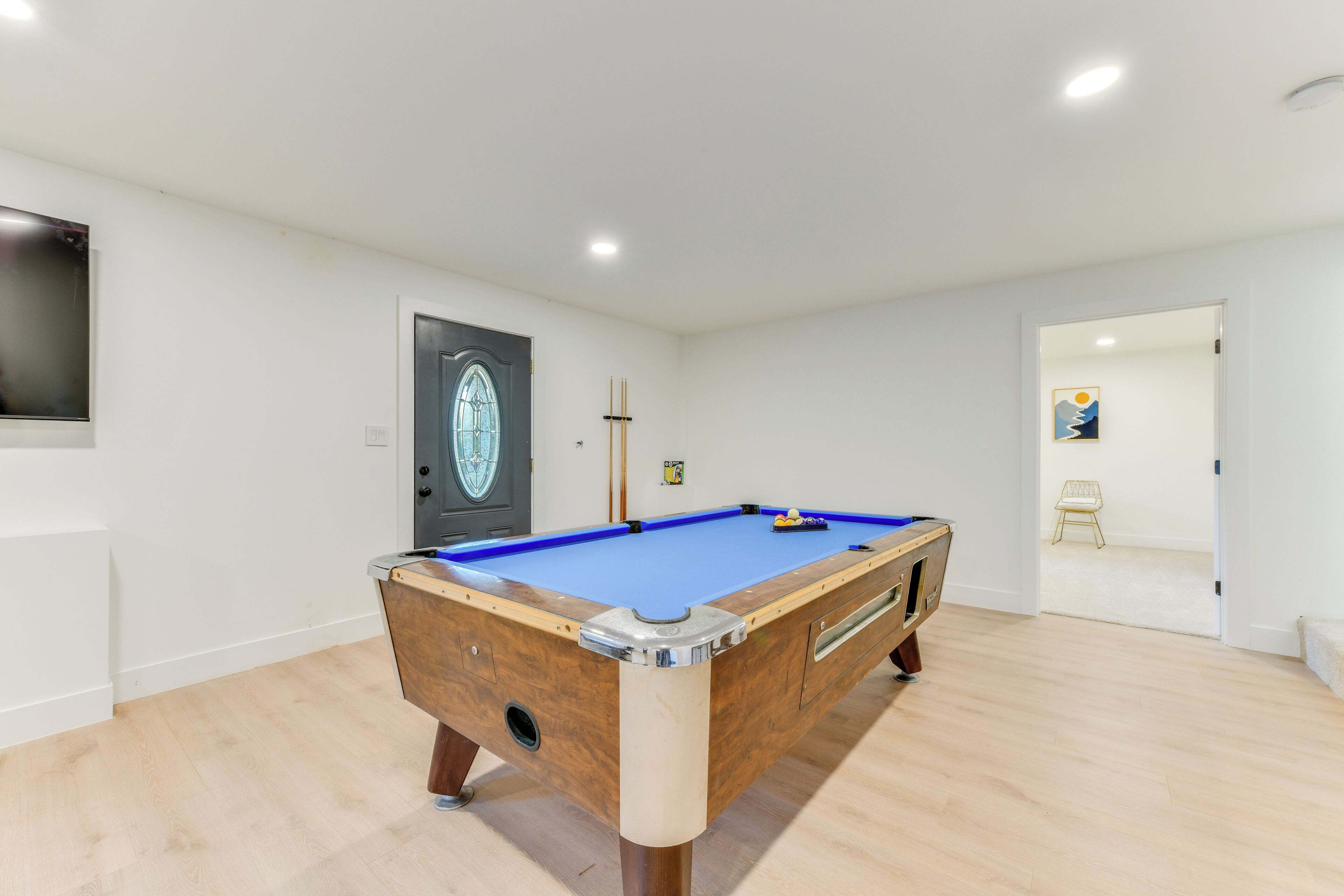 A pool table in a room with white walls and wooden flooring.