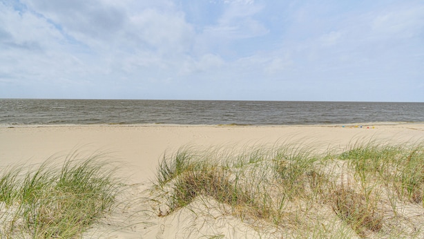 A beach with sand and grass in the foreground, and the ocean in the background.
