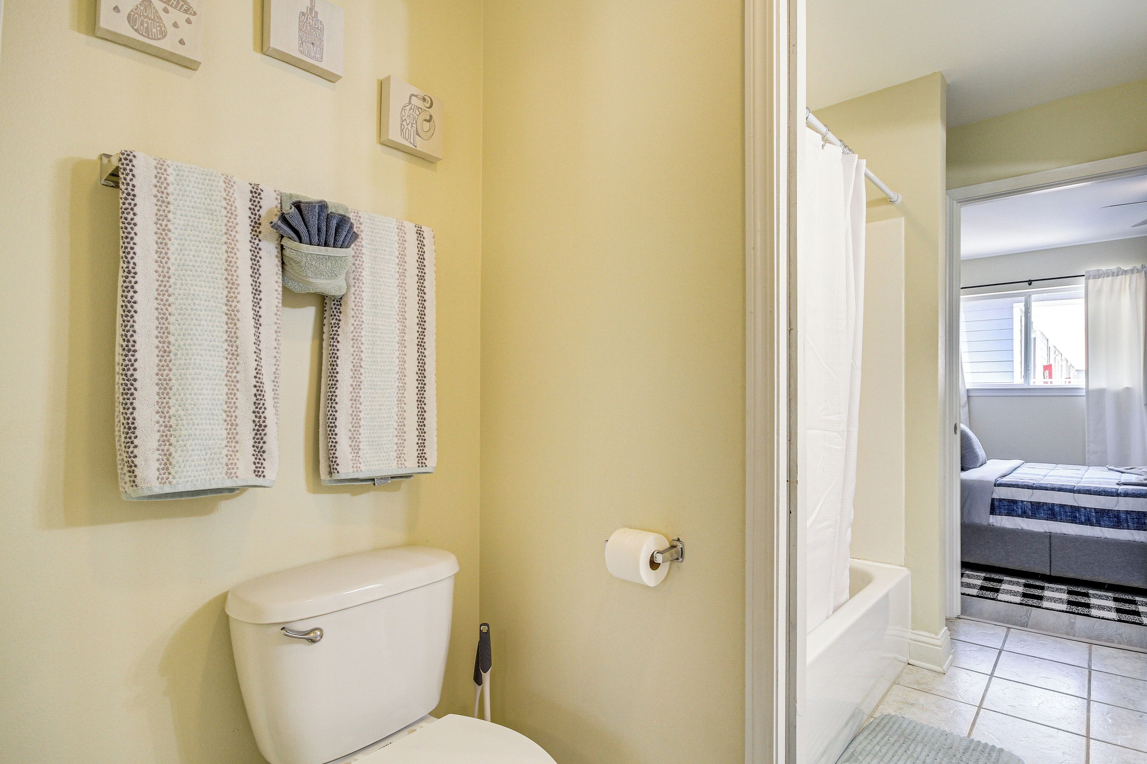 A bathroom with a toilet, two patterned towels, a roll of toilet paper, and a shower area visible through an open door.