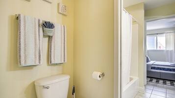 A bathroom with a toilet, two patterned towels, a roll of toilet paper, and a shower area visible through an open door.