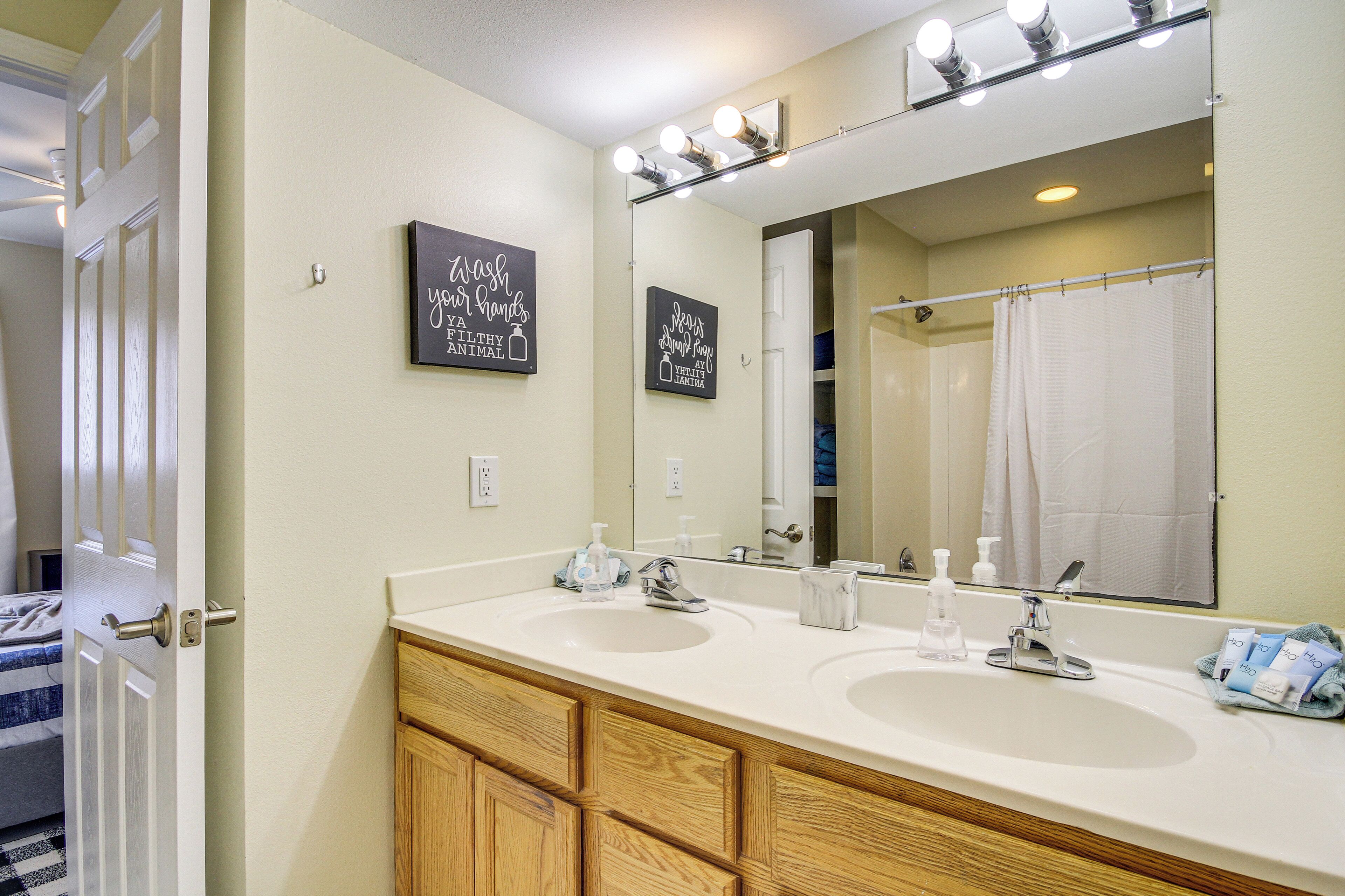Un baño con dos lavamanos, armarios de madera, un espejo grande con luces y decoración inspiradora en la pared.