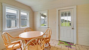 A dining area with a round wooden table and wicker chairs, a white door, and windows with views of a backyard. - Spacious Owensville Getaway w/ Winery On-site! (Rosebud)