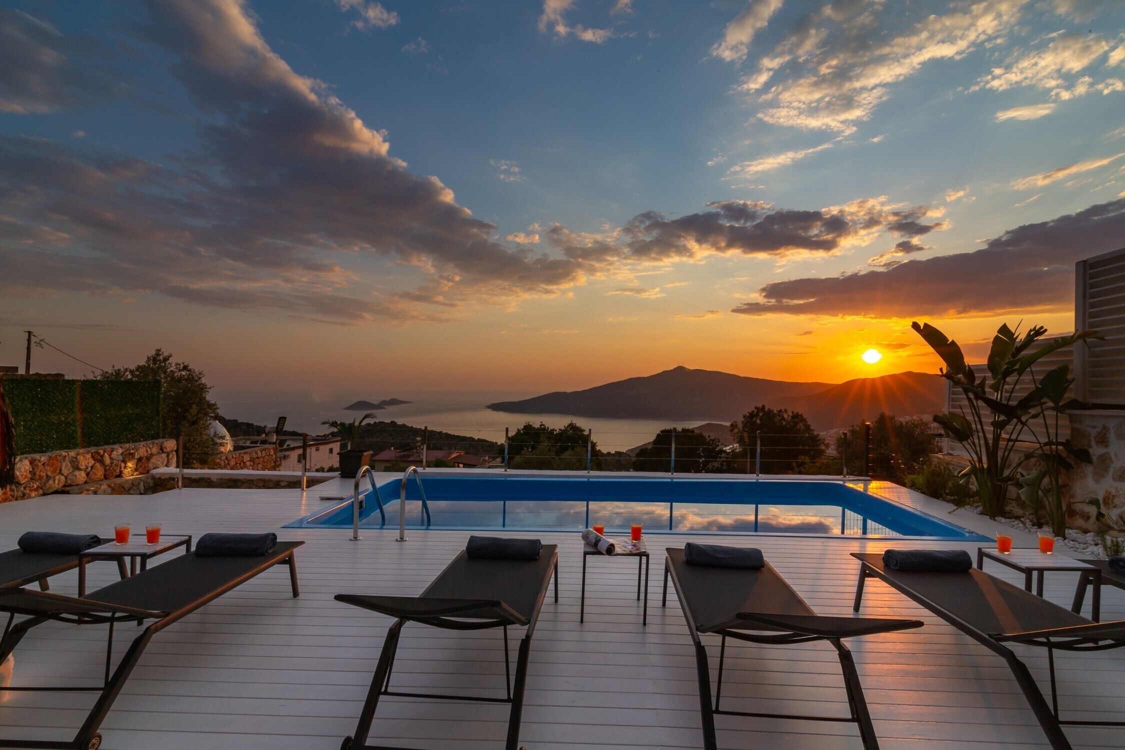 Area piscina con lettini e vista del tramonto sul mare.