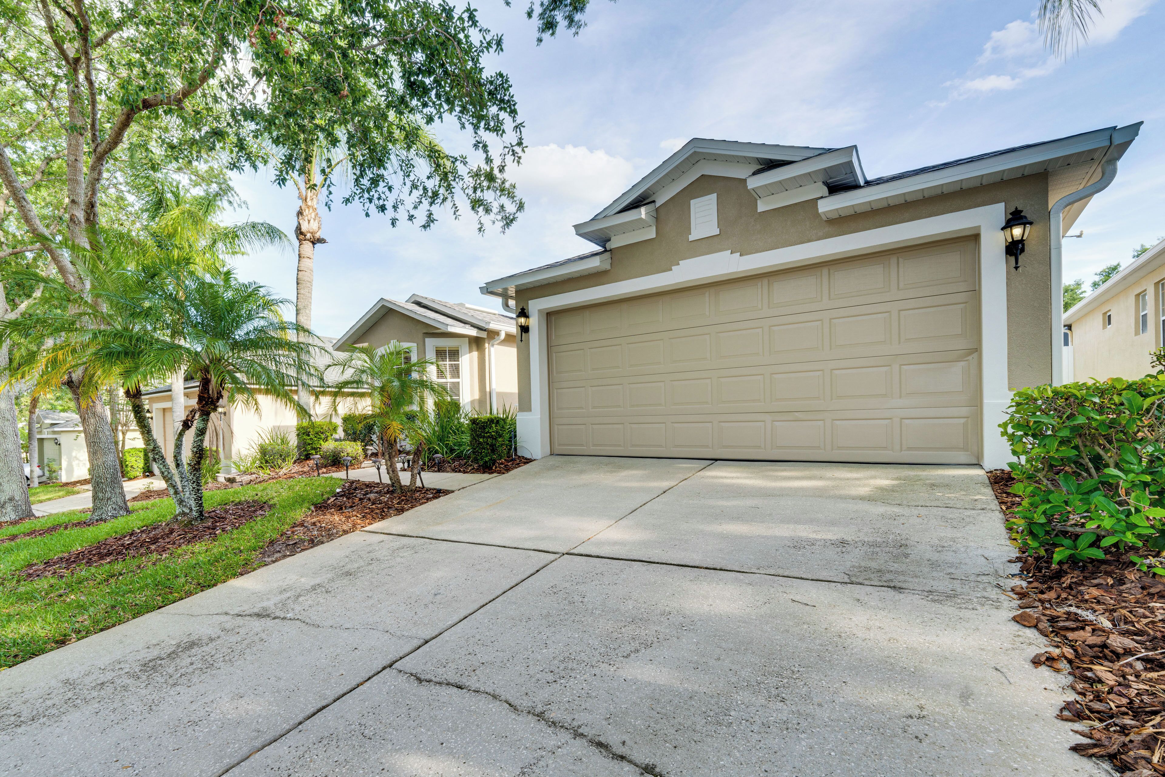 A residential driveway with a garage, palm trees, and a well-maintained lawn.