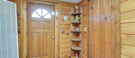 Interior de madeira com uma porta, um pequeno estante com objetos decorativos e um extintor de incêndio no chão.