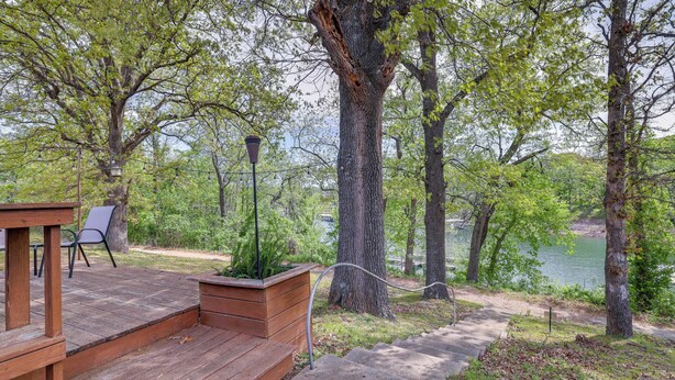 Una terraza de madera con escalones que conducen a un espacio de descanso, rodeada de árboles y vista a un lago.