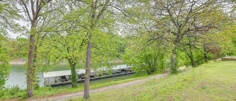 A riverside area with a dock and a small building, surrounded by trees and grassy banks.