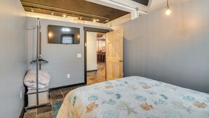 Une chambre à coucher comprenant un lit, une télévision, une porte en bois et un couloir menant à une salle à manger.