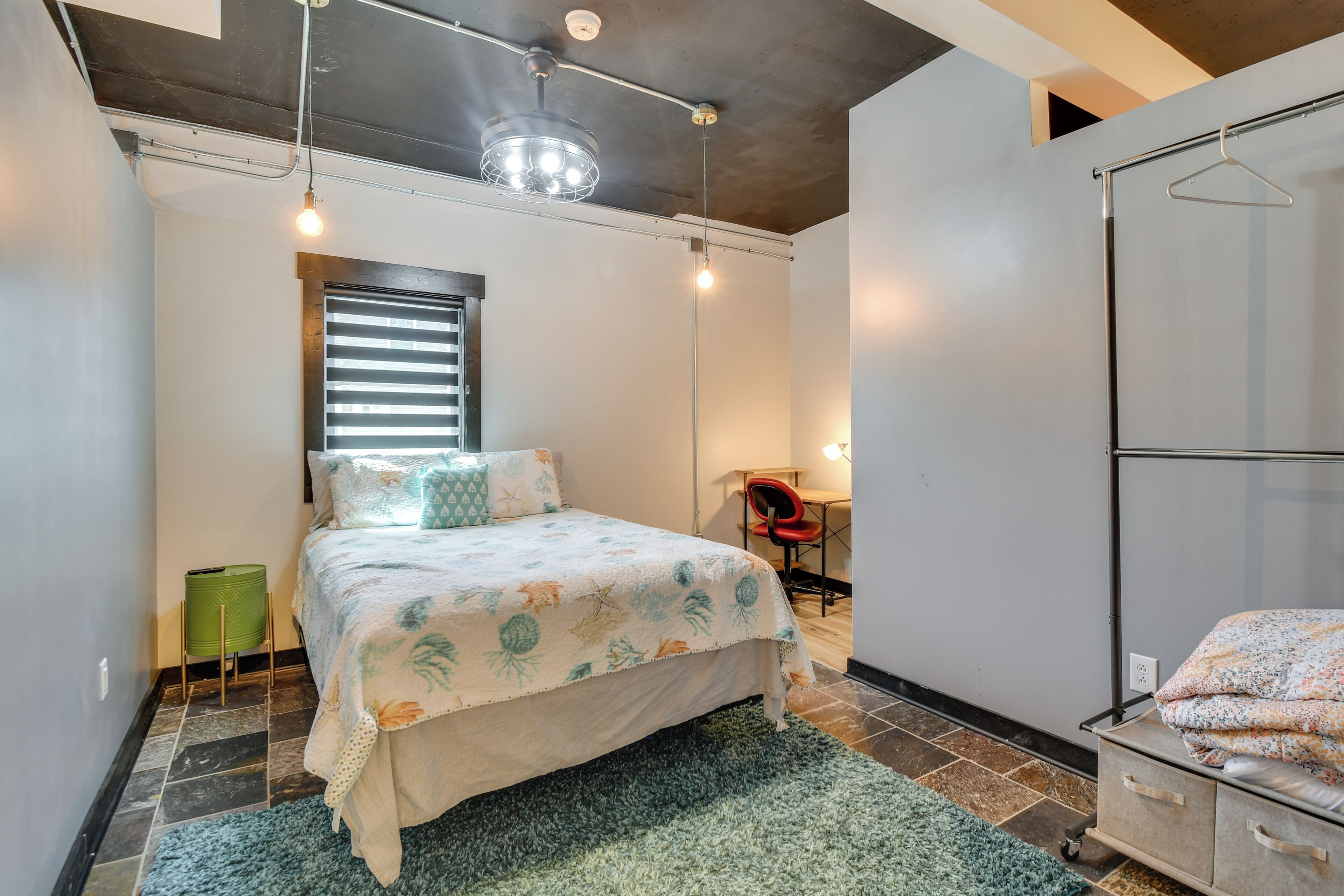 A bedroom with a bed, a hanging light fixture, a window with blinds, a chair, and a wardrobe.
