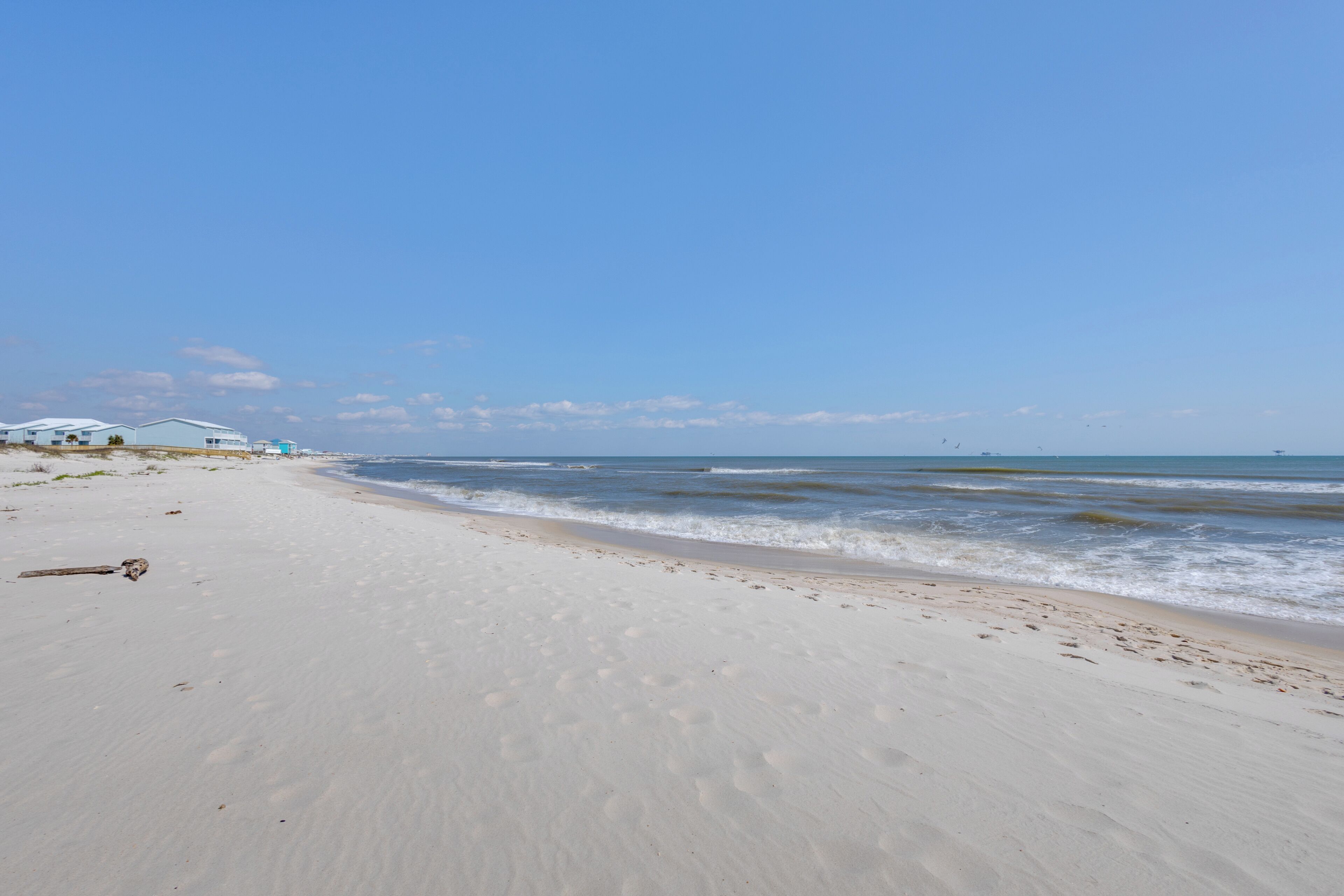 Una spiaggia con una riva sabbiosa, alcune impronte e una struttura sullo sfondo.