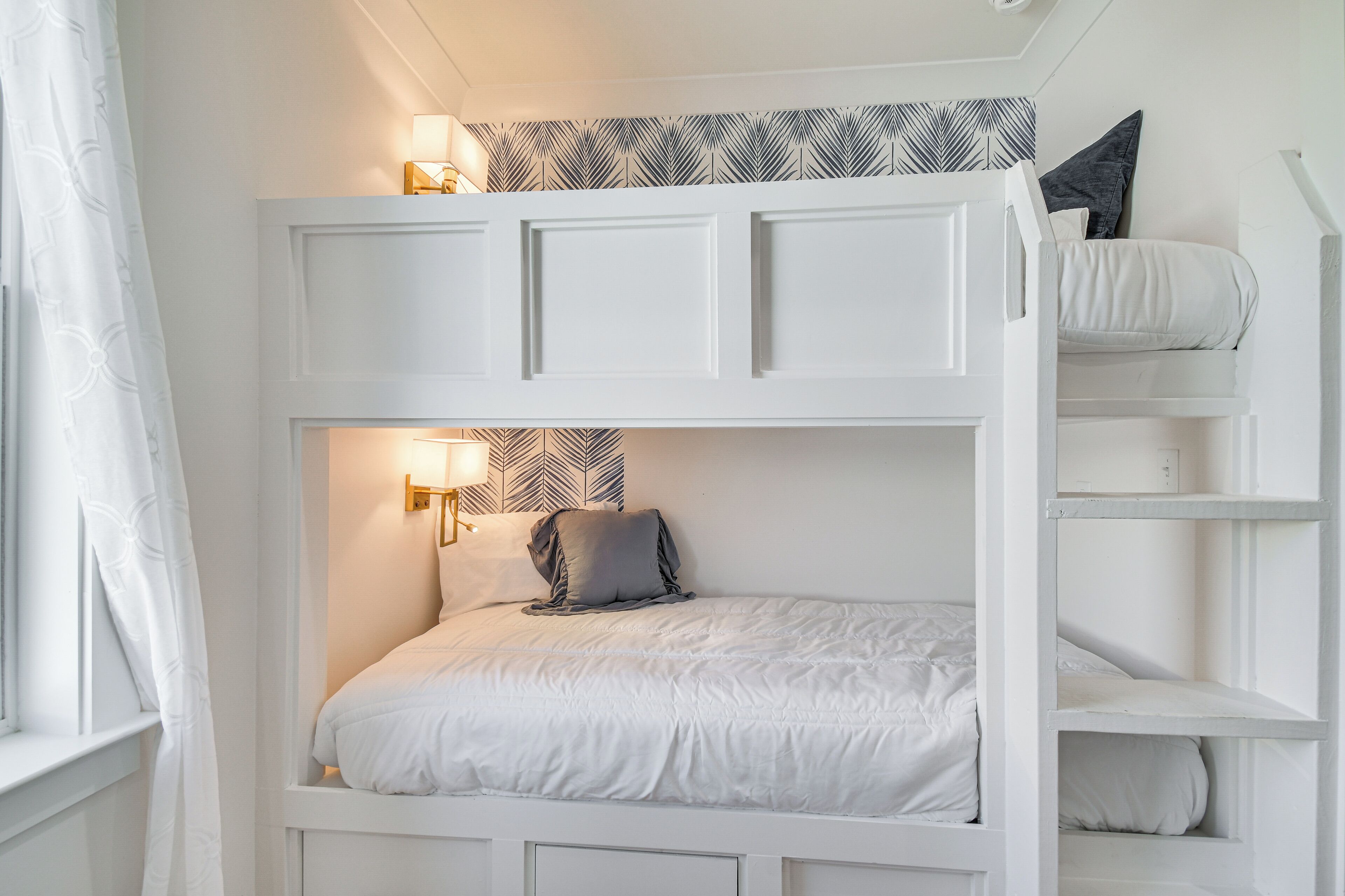 Un lit superposé avec une tête de lit, une table de chevet avec une lampe et un mur décoré d’un motif.
