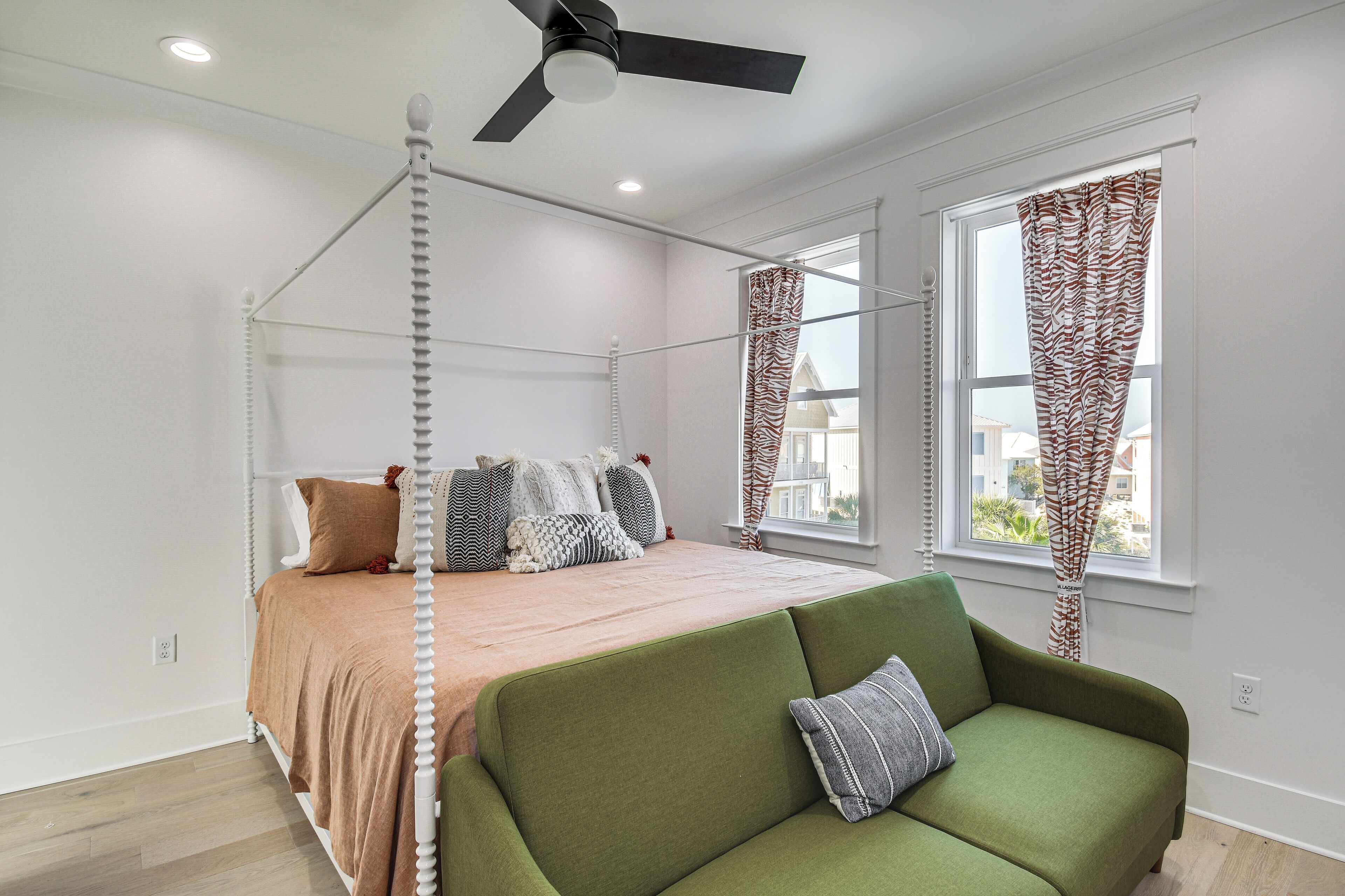 A four-poster bed with a brown bedspread, a green sofa with a pillow, and a ceiling fan.