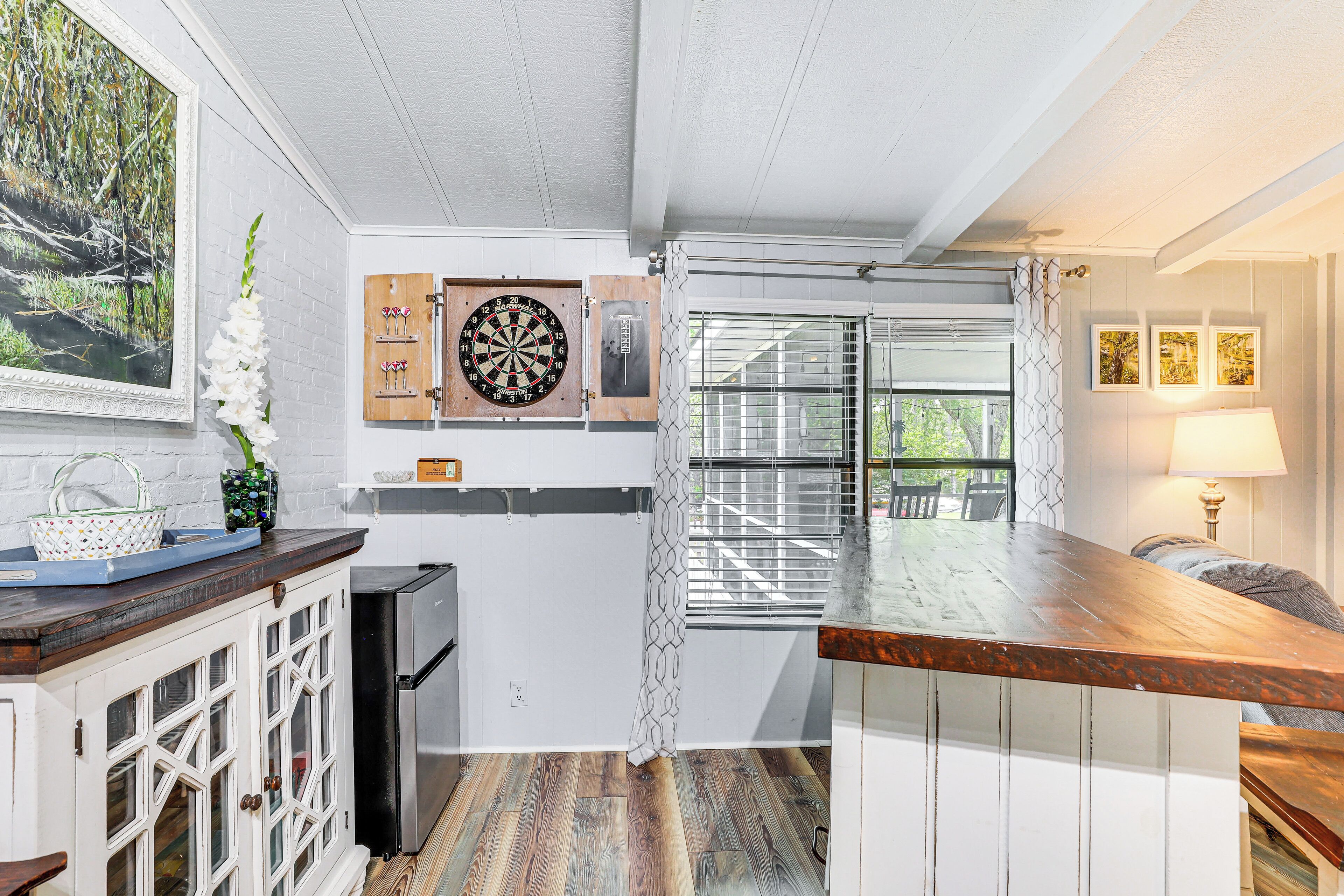 A kitchen with wooden cabinets, a refrigerator, a dartboard, and a window with blinds.