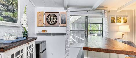 A kitchen with wooden cabinets, a refrigerator, a dartboard, and a window with blinds.