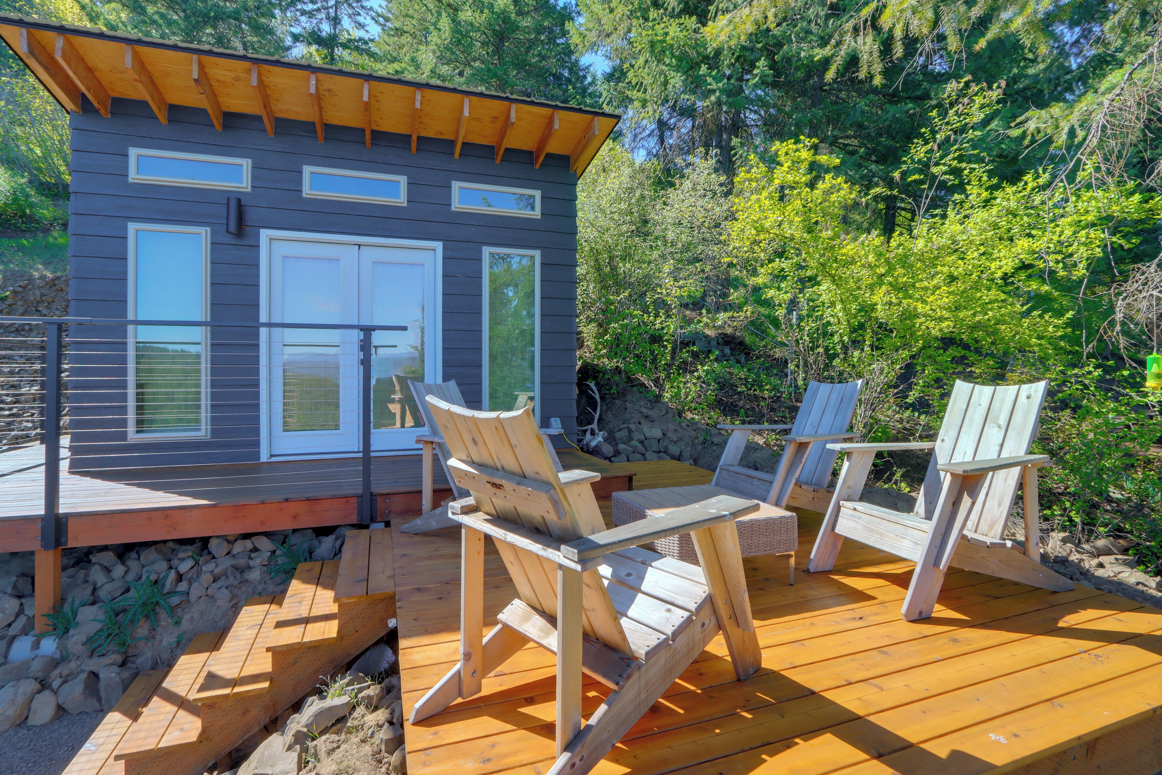 A wooden deck with Adirondack chairs and a small building with large windows.