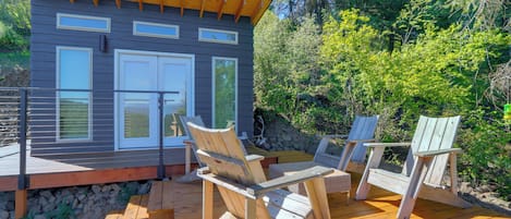 A wooden deck with Adirondack chairs and a small building with large windows.