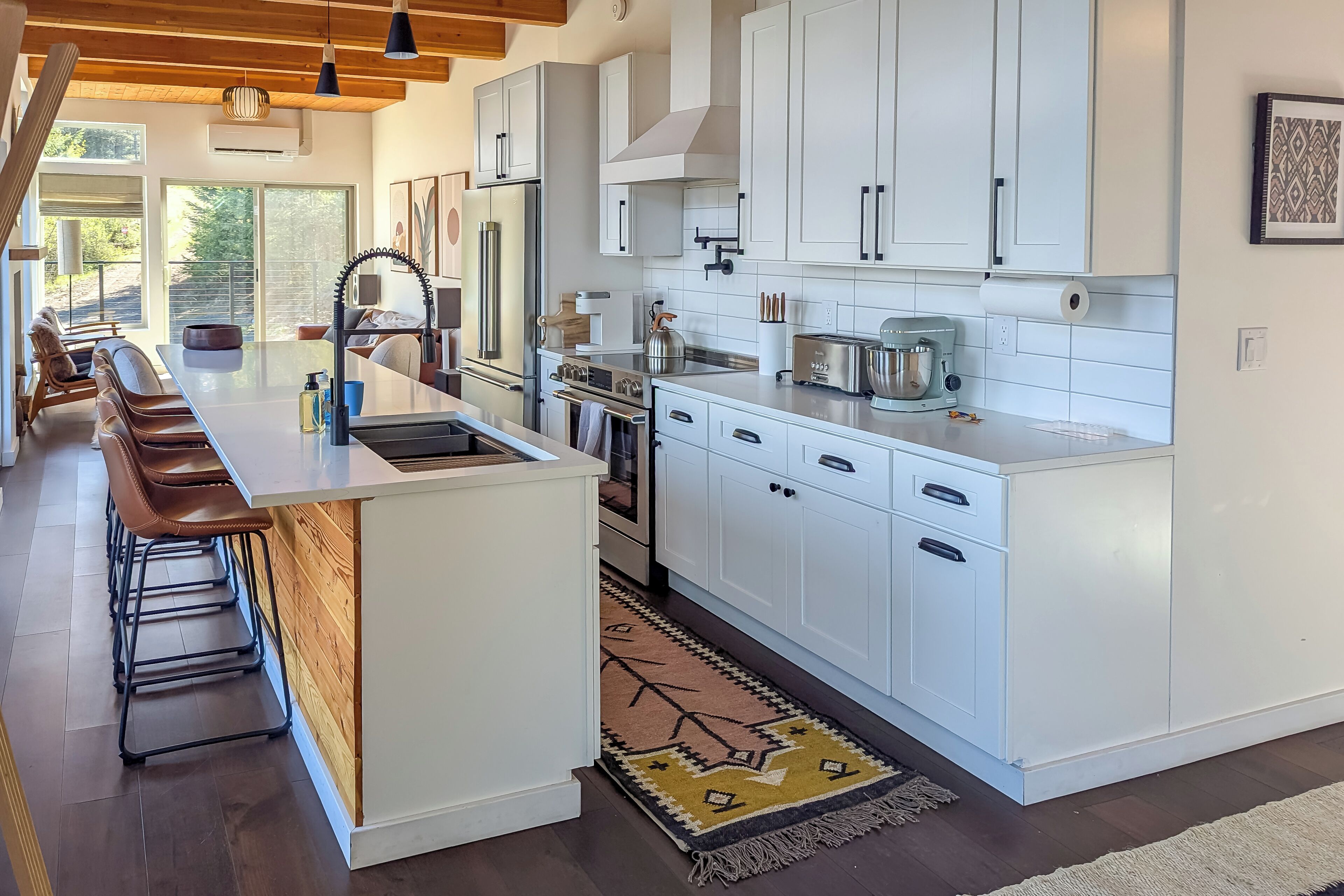 Una cocina moderna con armarios blancos, electrodomésticos de acero inoxidable y una isla central con taburetes de bar.