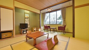 Ein traditioneller japanischer Raum mit Tatami-Boden, einem niedrigen Tisch, einem Fernseher und Blick ins Freie.