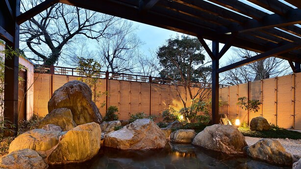 Ein ruhiger Garten mit Teich, großen Felsen und Bambuspflanzen.