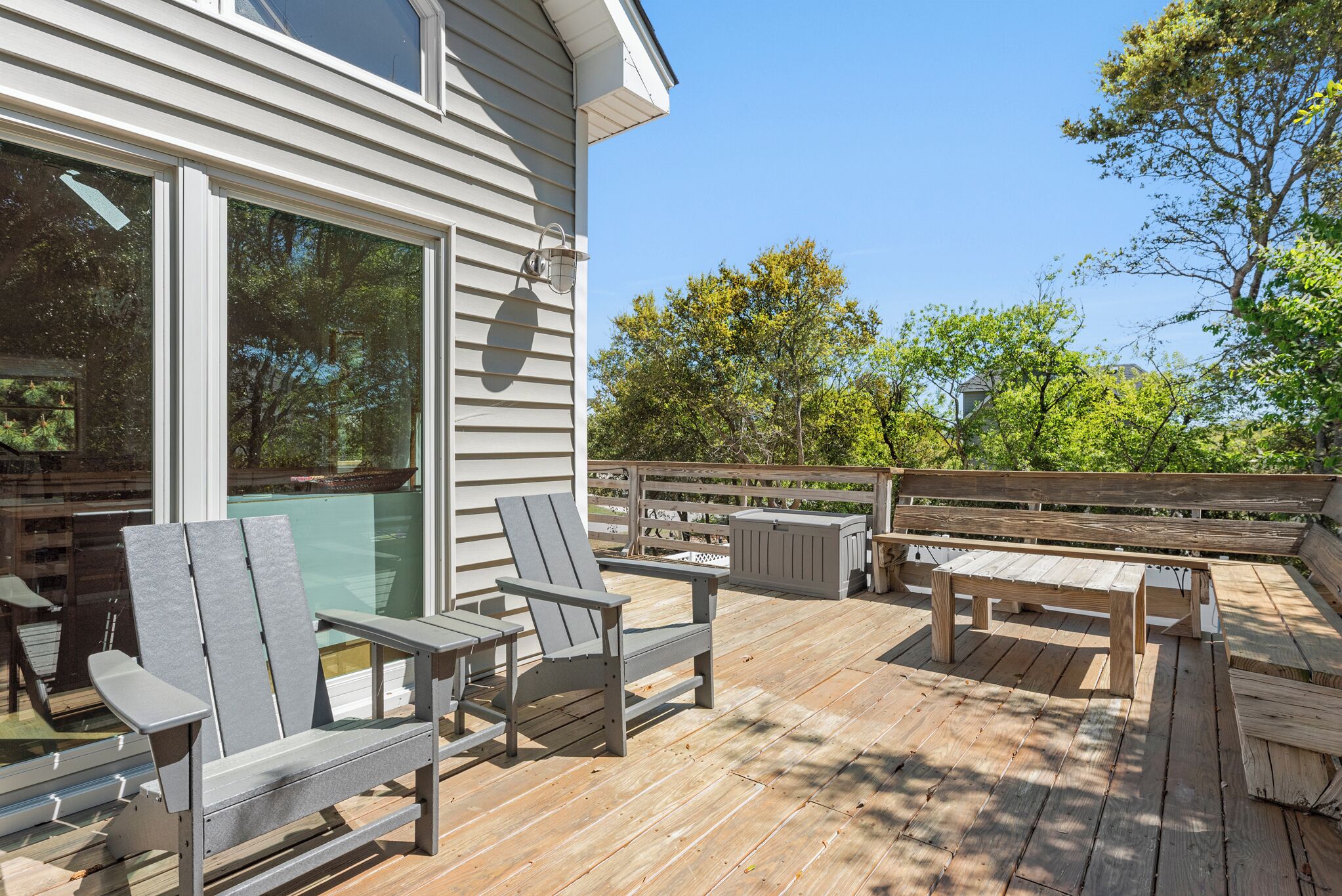 A wooden deck with Adirondack chairs, a picnic table, and a glass enclosure.