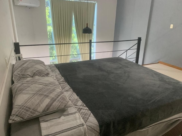 A bed with a black mattress and grey bedding, a black metal headboard, and a window with curtains.