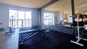 A spacious gym with large windows, various exercise equipment, and a mirrored wall. - São Sebastião ap 210 -flet com hidro (Jaragua do Sul)