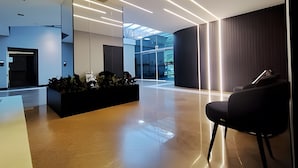 A modern lobby with a reception desk, a black chair, and a plant arrangement. - São Sebastião ap 210 -flet com hidro (Jaragua do Sul)