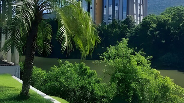 A modern building with a glass facade, surrounded by lush greenery and a body of water. - São Sebastião ap 210 -flet com hidro (Jaragua do Sul)