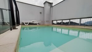 A rooftop swimming pool with clear water, a glass balustrade, and a view of distant buildings. - São Sebastião ap 210 -flet com hidro (Jaragua do Sul)