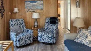 A living room with wooden paneling, a ceiling fan, two patterned armchairs, a sofa, and a small table with lamps. - 1050 Ocean Lakes Pet Friendly Golf Cart⛱️🏝️🩱🌊👙☀️🐚 (Myrtle Beach)