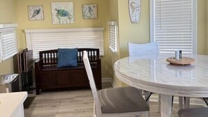 A dining area with a round table and four chairs, a sofa with a blue pillow, and three wall-mounted artworks. - 1050 Ocean Lakes Pet Friendly Golf Cart⛱️🏝️🩱🌊👙☀️🐚 (Myrtle Beach)