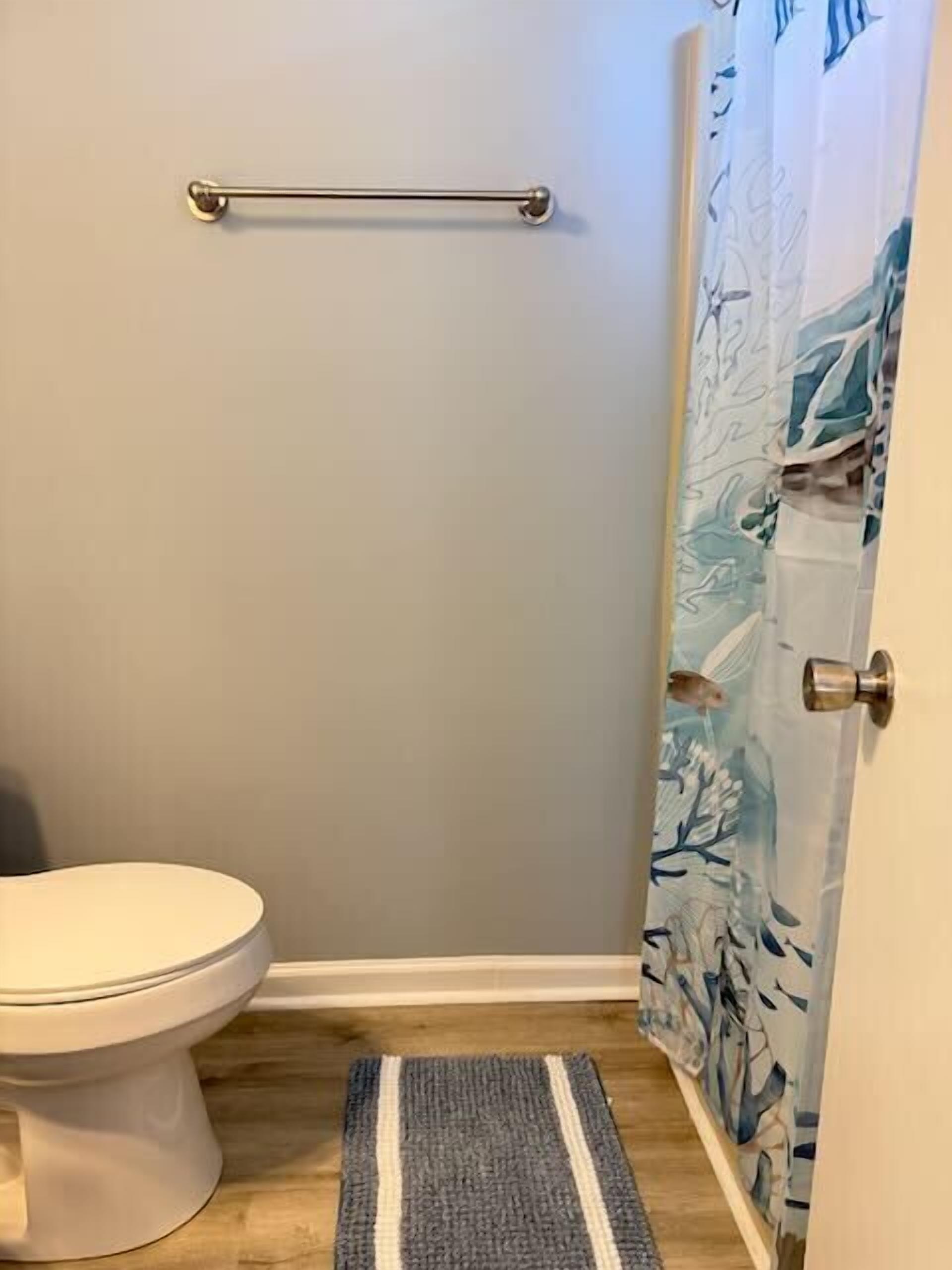 Une salle de bain équipée de toilettes, d’une barre d’appui, d’un rideau de douche à motifs marins et d’un plancher en bois.