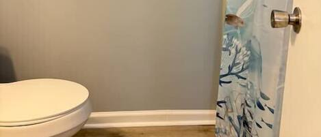 Une salle de bain équipée de toilettes, d’une barre d’appui, d’un rideau de douche à motifs marins et d’un plancher en bois.
