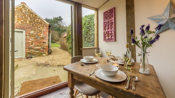Un coin repas avec une table dressée pour deux personnes, un bâtiment en pierre à l’extérieur et une étoile décorative sur le mur.