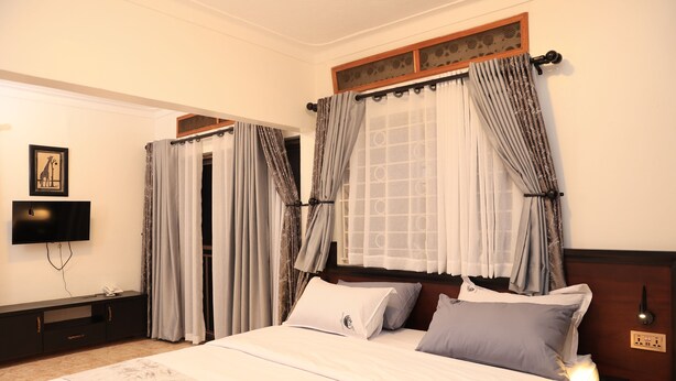 Una habitación de hotel con cama, cortinas, televisor y un enchufe en la pared.