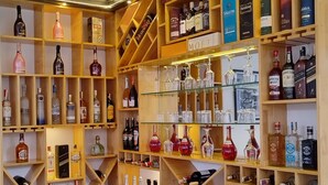 Zona de bar con estantes llenos de botellas de licores y vasos.