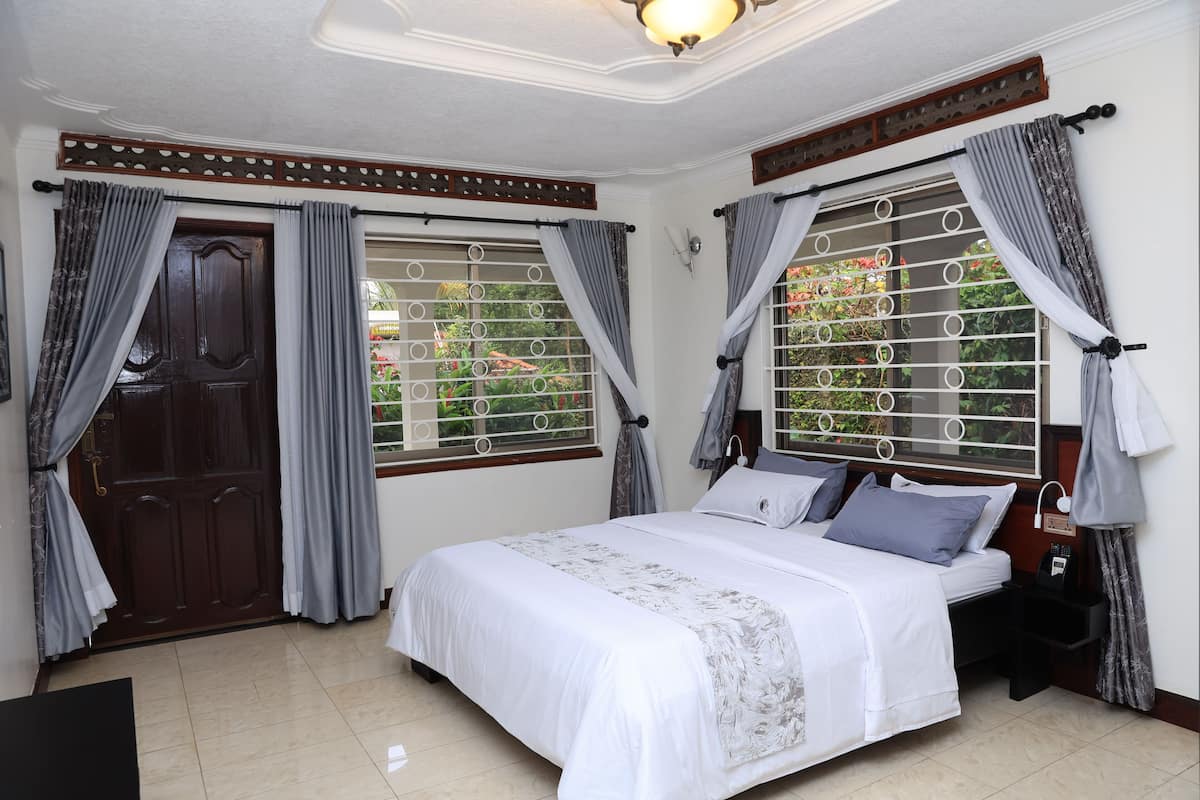 Une chambre à coucher avec un lit, des rideaux, une porte en bois et une fenêtre avec une grille en métal.
