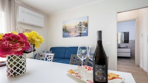 Un tavolo da pranzo con una bottiglia di vino, un bicchiere e un piatto con cibo. Si vede un divano blu e un quadro appeso al muro.