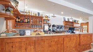 A wooden counter with a coffee machine, shelves with bottles, and a display of croissants.