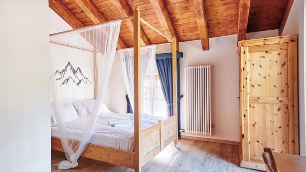 A wooden-framed bedroom with a four-poster bed, a radiator, and a wooden wardrobe.