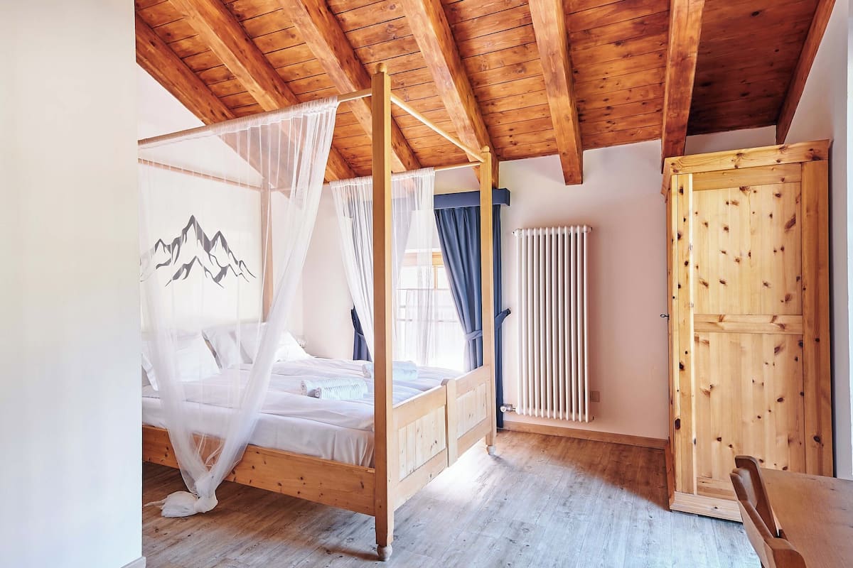 A wooden-framed bedroom with a four-poster bed, a radiator, and a wooden wardrobe.