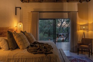 Une chambre avec un grand lit, une chaise, une lampe et une vue sur l’extérieur.