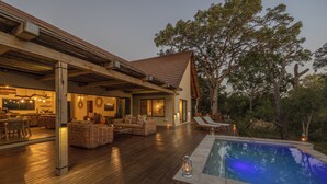 Um deck de madeira com piscina, área de estar externa e espaço coberto com espaço de refeições.