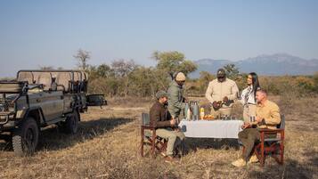 A group of people seated around a table in an outdoor setting with a vehicle nearby.